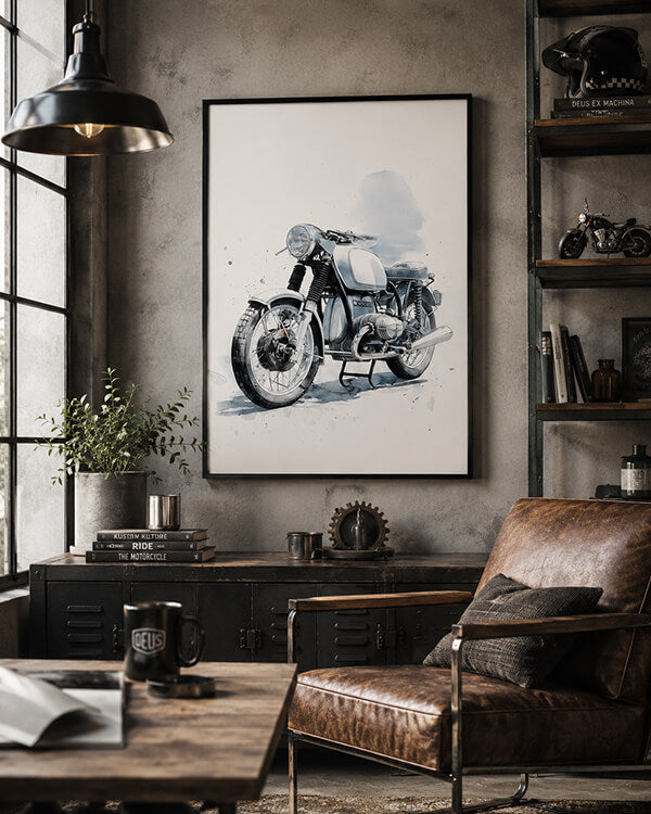 A framed black and white watercolor-style motorcycle print hangs on a textured gray wall in a rustic, industrial-themed room with a brown leather armchair, wooden table, and shelving.
