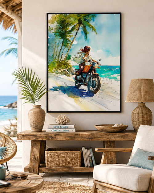 A framed vertical watercolor painting of a woman riding an orange motorcycle on a tropical beach with palm trees and turquoise ocean, displayed on a beige wall above a rustic wooden console table in a styled living room.