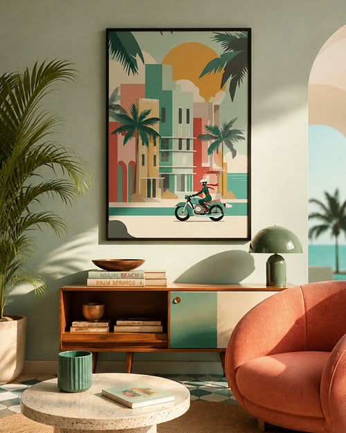 A framed retro-style art print depicting a beach town with palm trees, colorful buildings, and a motorcyclist, displayed on a wall in a modern living room setting.